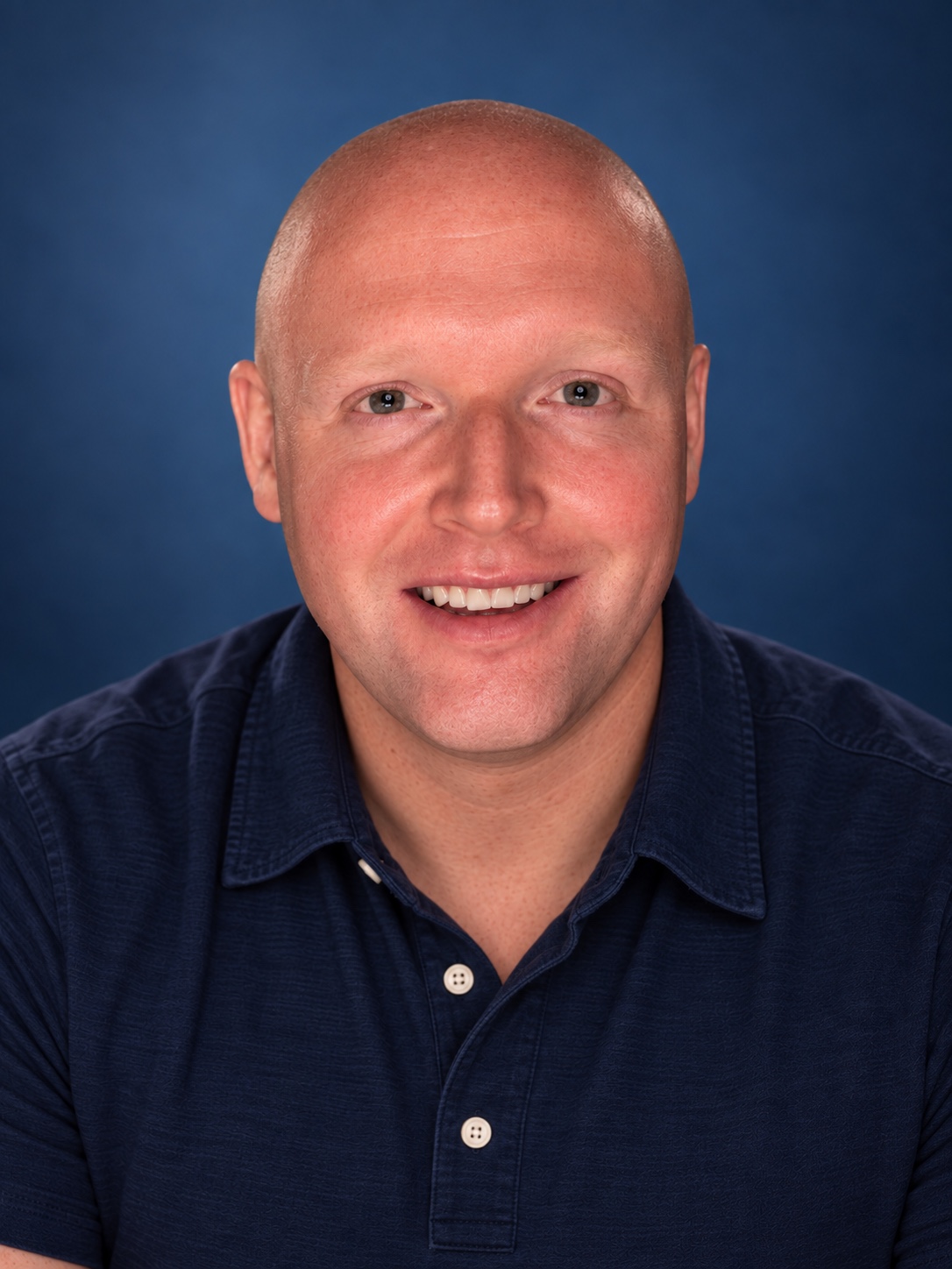Andy Frey smiling in a navy polo against a blue studio background